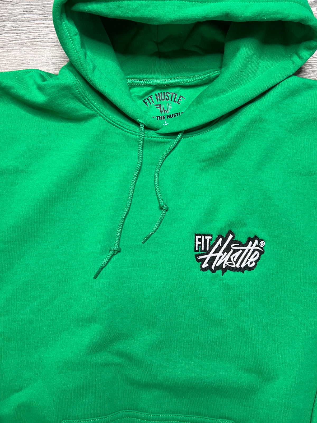 A bright green pullover hoodie laid flat on a light wood surface, featuring a black and white embroidered 'FIT Hustle' logo on the left chest and matching green drawstrings.