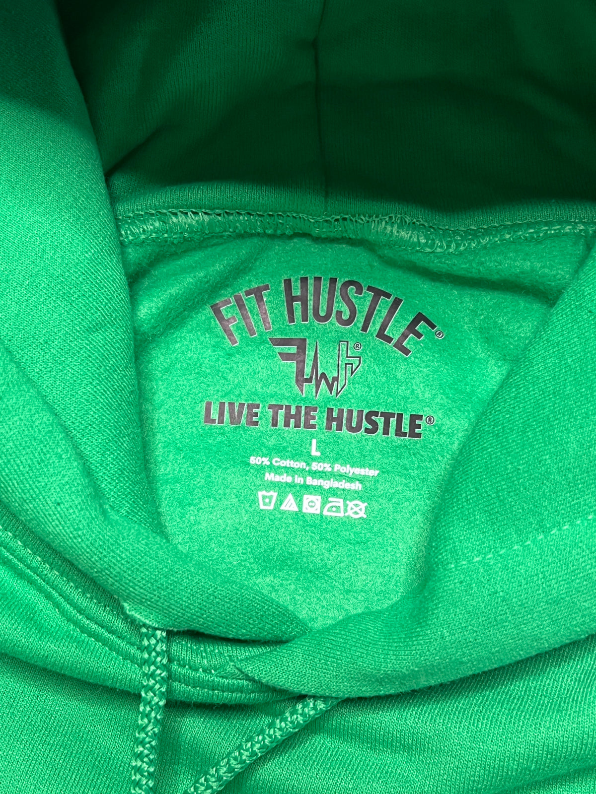 Close-up of the inside hood lining of a bright green hoodie, showing the printed brand name 'FIT HUSTLE' and 'LIVE THE HUSTLE' in dark red text.