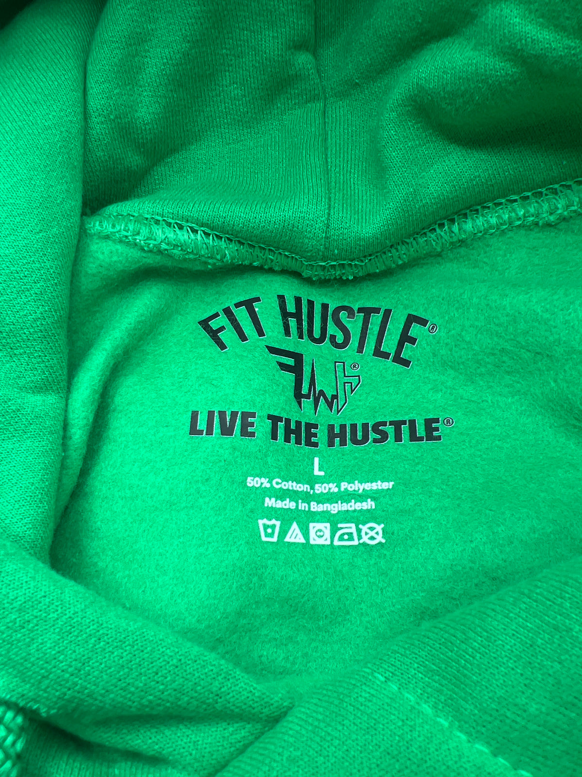 Close-up of a bright green hoodie showing the inner neck label with the text 'FIT HUSTLE' and 'LIVE THE HUSTLE' printed in black and white.